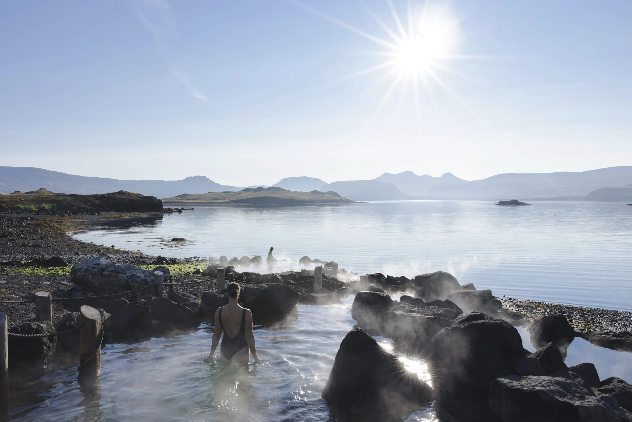 Bathers in a hot spring at the edge of Hvalfjörður, with mountains and low sun beyond